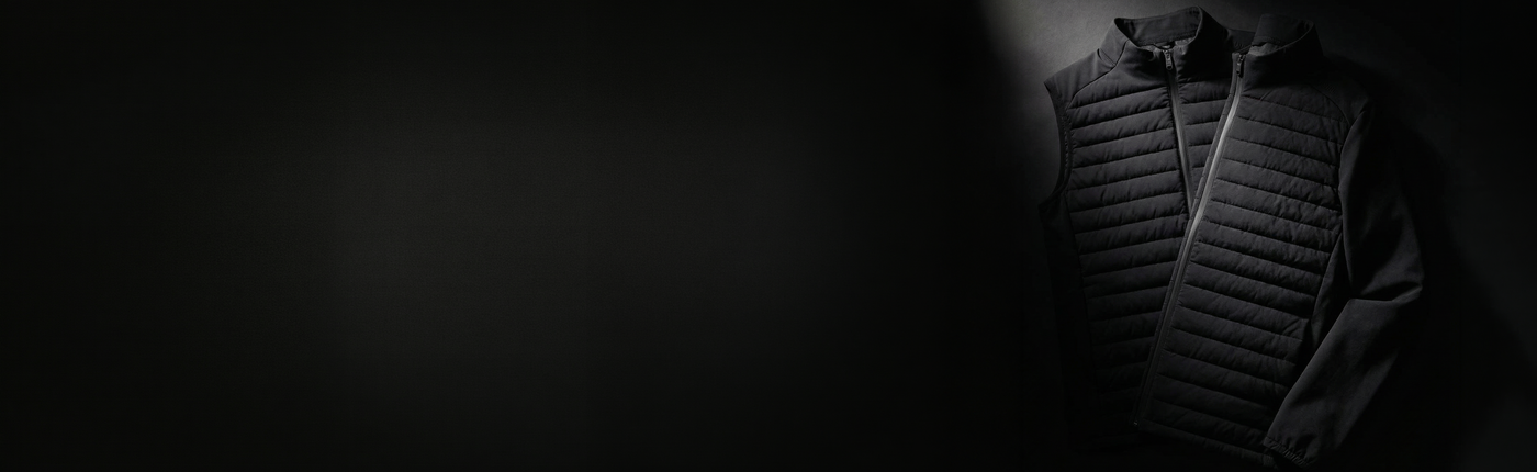 A black quilted zip-front vest with a hood, shown in dramatic side lighting against a dark black background.